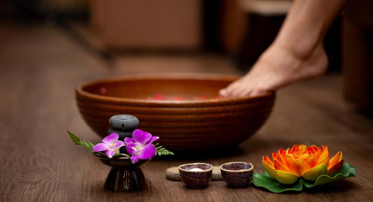 A person about to dip their foot into a bowl, accompanied by flowers and salts